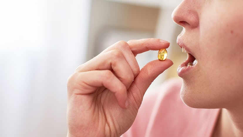 a woman takes a tablet with fish oil in capsules. the girl brings the yellow capsule to her mouth