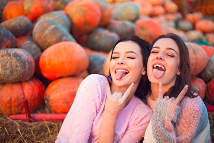 Fashionable beautiful young girlfriends together at the autumn pumpkin patch background. Having fun ...
