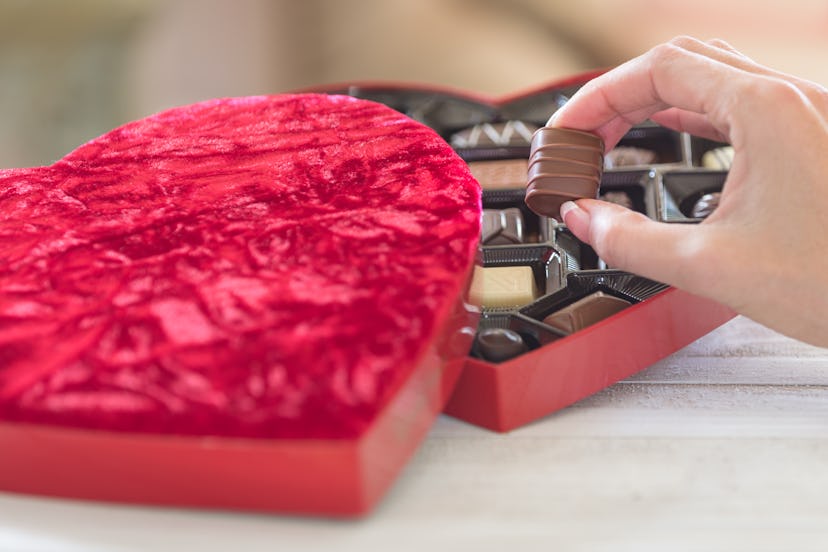 Hand taking a truffle ot of a heart shaped box of chocolates day