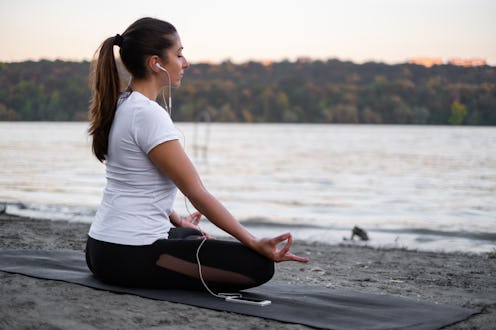Beautiful young woman is practicing meditation on the river bank