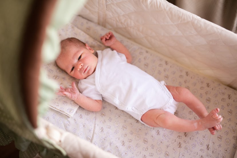 Newborn baby boy in bed. New born child in white bodykit lying in light cradle. Children sleep. Bedd...