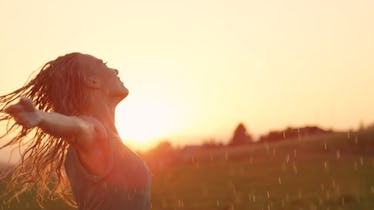 CLOSE UP, LENS FLARE, COPY SPACE: Smiling young woman spins in the rain with her arms outstretched. ...