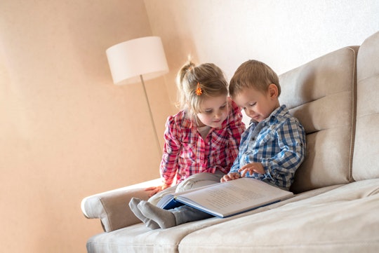 Cute little brother and sister reading book together on couch at home