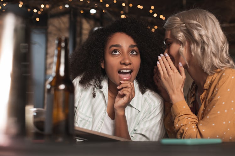 Gossip lover. Pretty curly woman sitting at the bar counter next to her friend listening to her whis...