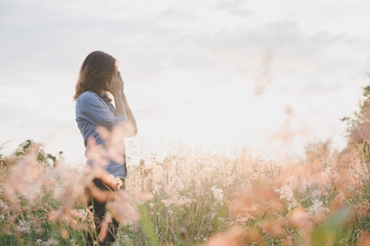 Sad woman standing in field with sunset background.