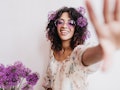 Attractive african girl having fun during photoshoot with flowers at home. Indoor portrait of dreamy...