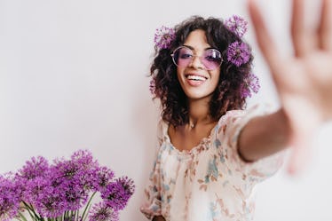 Attractive african girl having fun during photoshoot with flowers at home. Indoor portrait of dreamy...