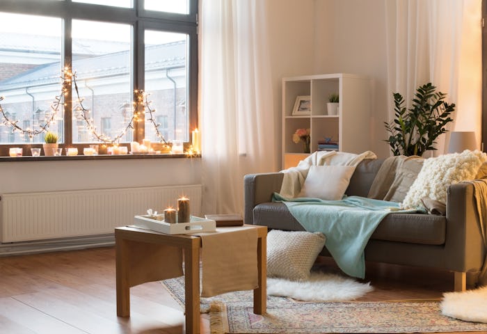 interior, christmas and interior concept - cushioned sofa, coffee table, garland string and candles ...