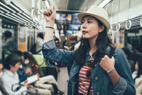 asian travel woman taking underground metro standing holding handle on train. female backpacker in s...