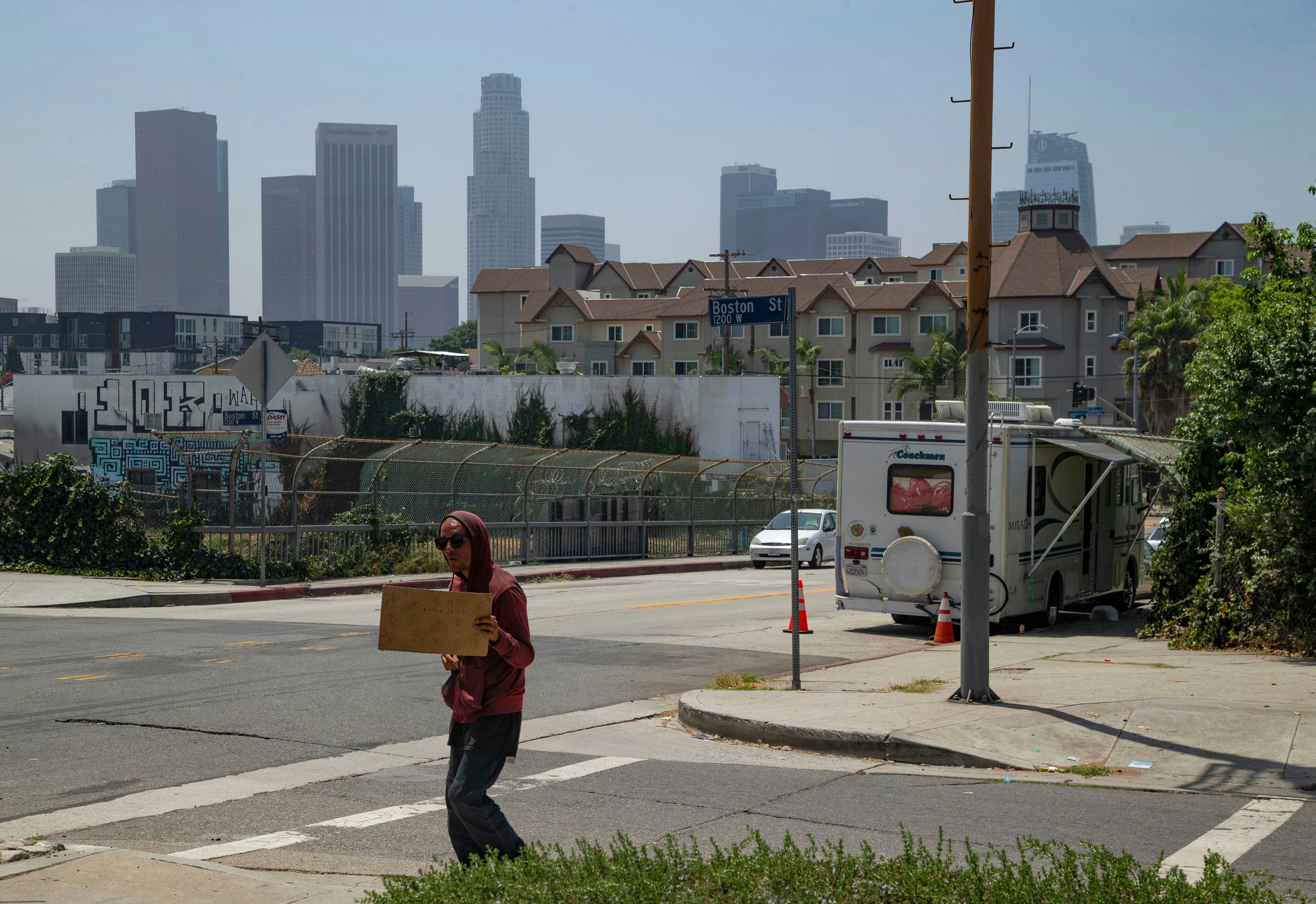 A homeless man pan handles next to a RV vehicle parked on an overpass of the CA-101 freeway in the E...