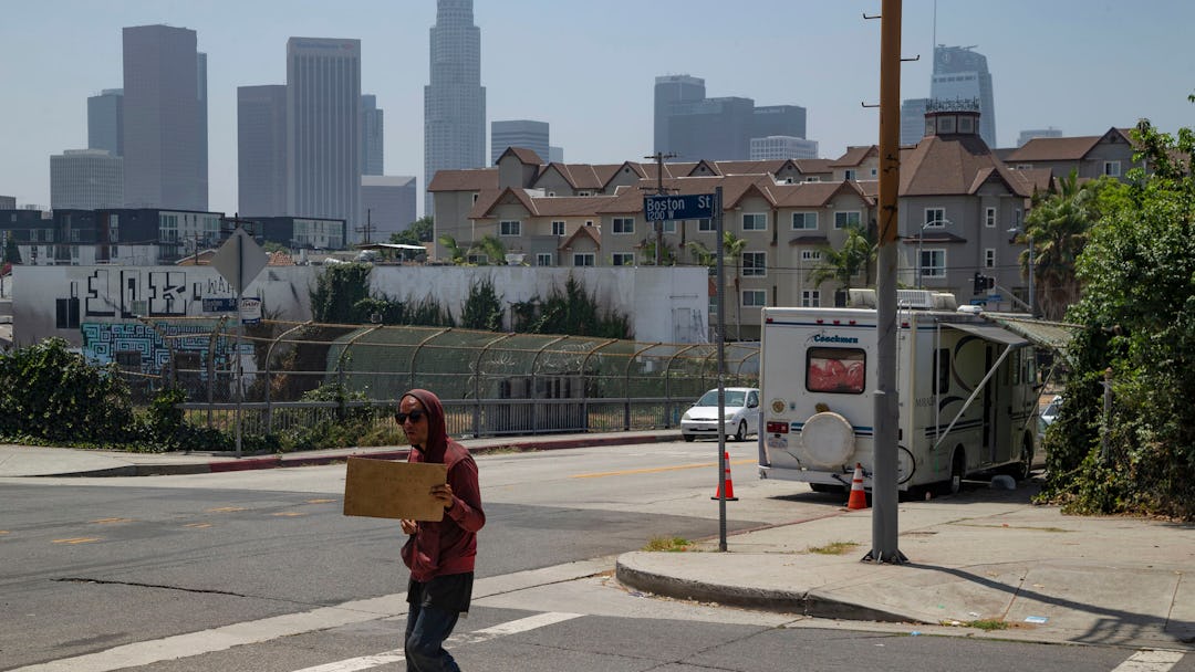 A homeless man pan handles next to a RV vehicle parked on an overpass of the CA-101 freeway in the E...