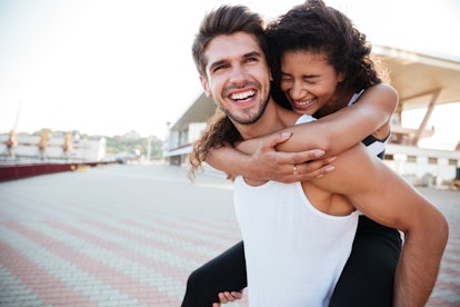 Smiling young man carrying woman on his back and laughing outdoors