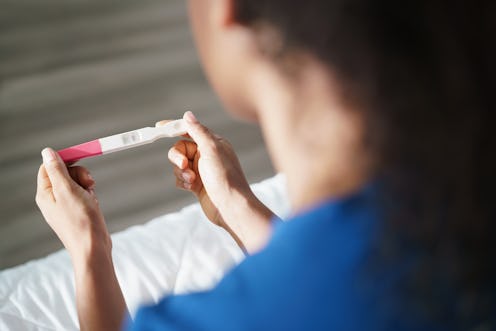 close up shot from over the shoulder woman sitting on bed looking at pregnancy test that's in focus