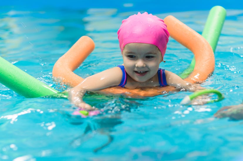 A little girl swimming in a pool with the help of two pool noodles 