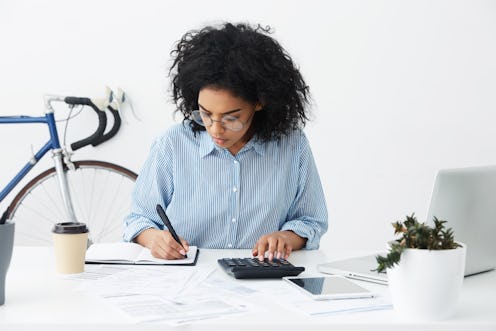 Portrait of attractive hardworking businesswoman with Afro hairstyle busy doing paperwork at office ...