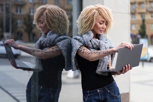 european hipster girl with tattoo on her hand and afro hairstyle work on laptop on street, in fresh ...
