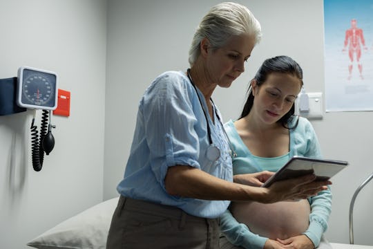 Front view of Caucasian female doctor discussing with pregnant woman over digital tablet in examinat...