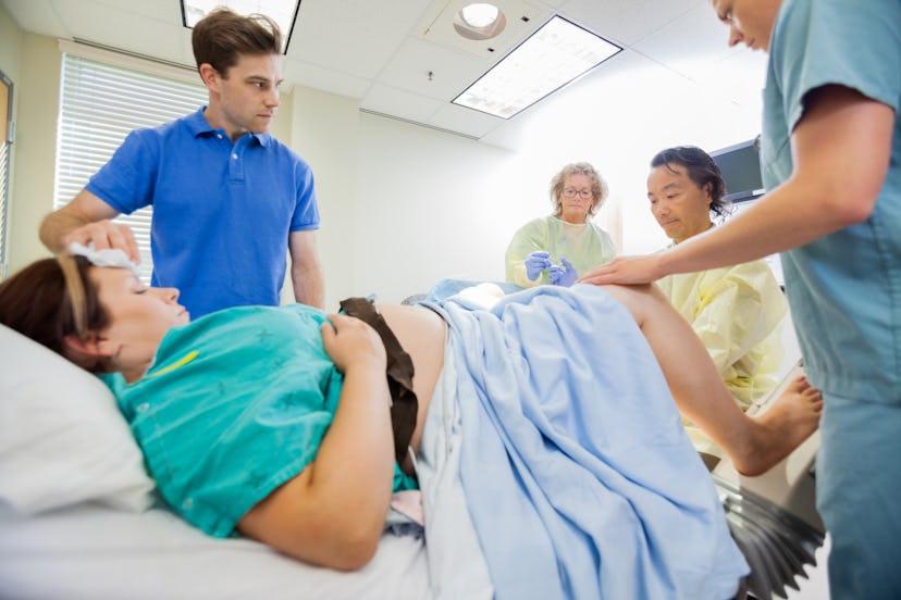 Mid adult man looking at medical team operating pregnant woman in hospital room