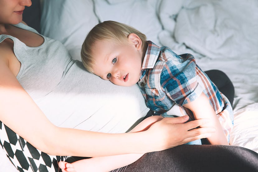 Pregnant mother and son are talking and spending time together in bed at home. Little child boy look...