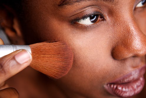 Close up side portrait of beautiful woman applying makeup with brush for smooth matte finish