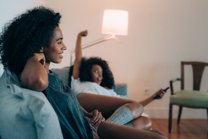 Happy young two black women lying down in the couch watching tv  
