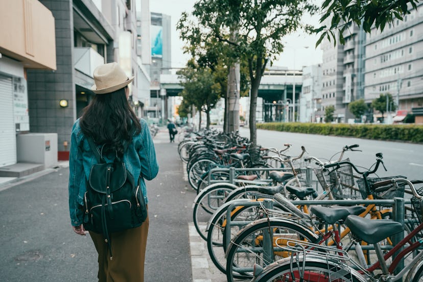 Back rear view of hipster girl walking on city street in osaka japan. young female backpacker in hat...