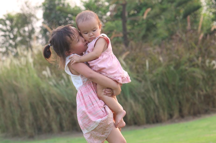 Two sisters are in the park with cute pink dress. They're love each other so much. The big sister is...