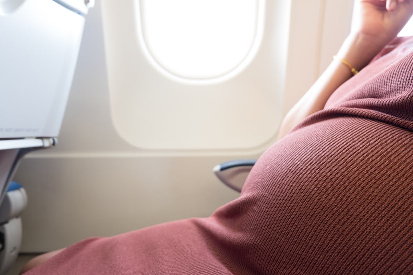 Happy pregnant woman is traveling to destination by plane sitting at window seat light are shining f...