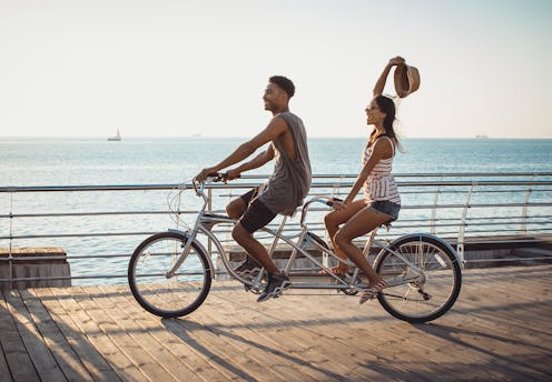 Portrait of a mixed race couple riding on tandem bicycle outdoors near the sea