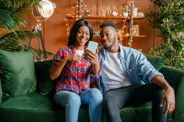 Black couple sitting on sofa and looking on phone