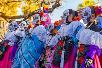 Group of unrecognizable women wearing traditional sugar skull masks and costumes for Dia de los Muer...