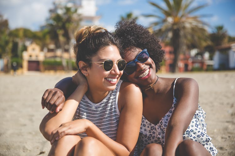 Two best friends smile and sit on a beach on a sunny day.