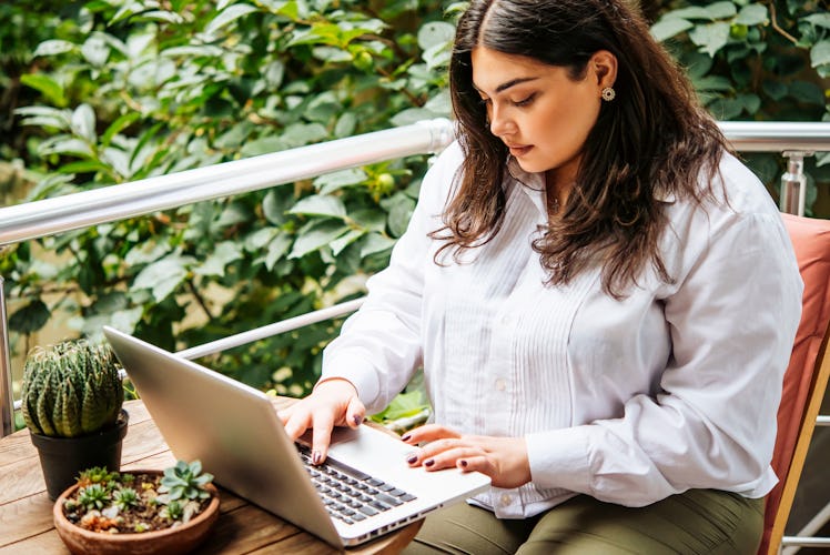 Portrait of beautiful plus size girl working on her laptop on balcony or terrace of cafe
