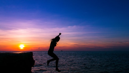 Silhouette of scared woman in the air falling from cliff into water at lovely colorful sunset in the...