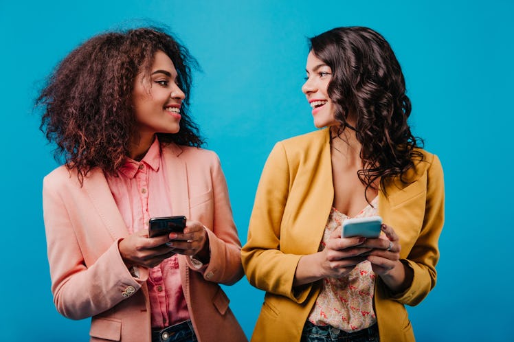 Adorable african girl texting message. Studio photo of two international friends with smartphones.