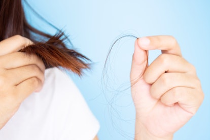Woman's hand holding hair falling from her head in white t-shirt with blue background. Young Asian f...