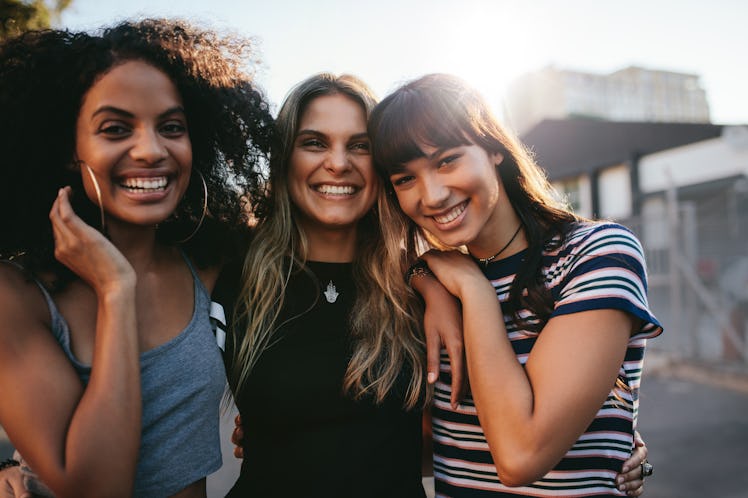 Outdoor shot of three young women having fun on city street. Multiracial female friends enjoying a d...