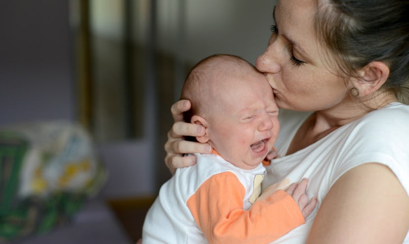 Close up of young mother holding her crying baby daughter, kissing her