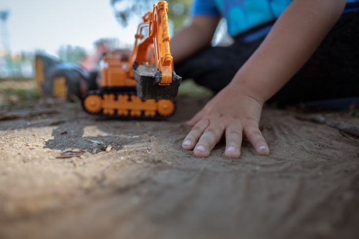 close up image of kid hands holding plastic tractor toy playing on dirt ground