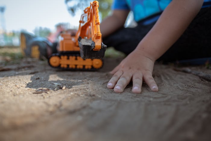 close up image of kid hands holding plastic tractor toy playing on dirt ground 