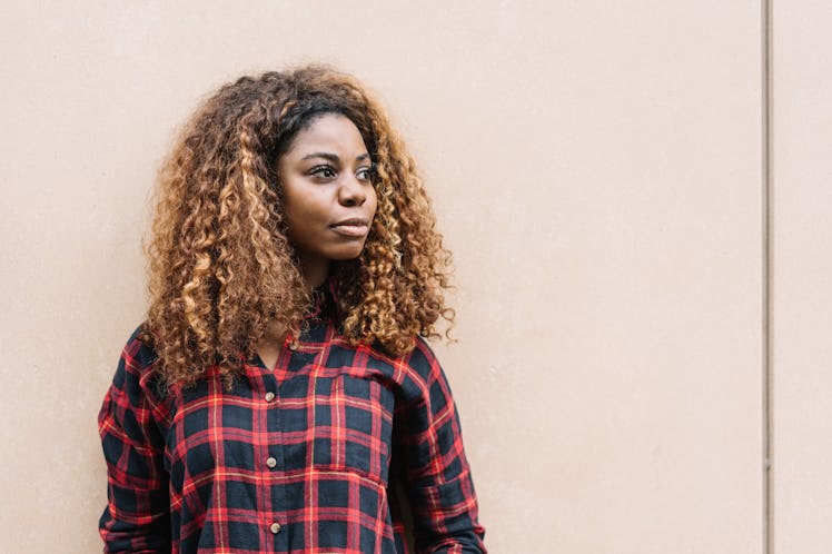 Portrait of young black woman wearing checked shirt looking away while standing against bright backg...