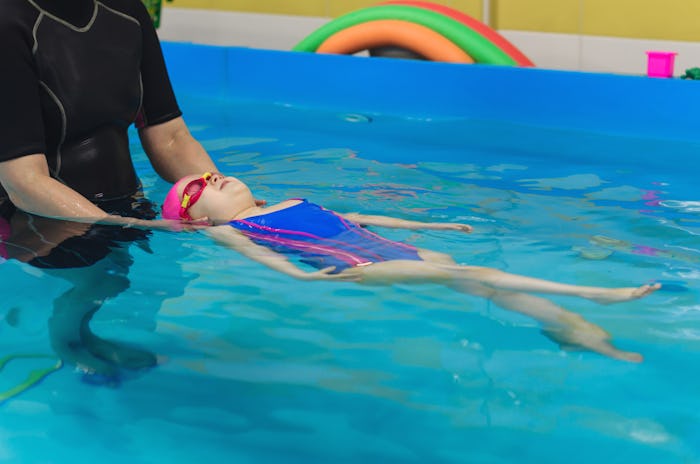 A little girl of European appearance in a pink rubber cap learning to swim in the pool