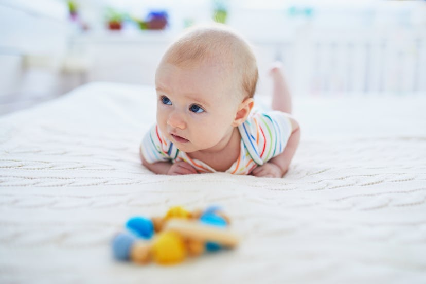 Adorable baby girl lying on bed on her tummy. Happy healthy little child practice crawling. Infant k...