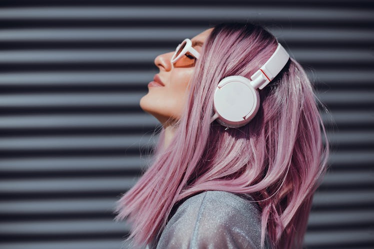 Beautiful young girl with purple pink hair listening to music on headphones, street style, outdoor p...