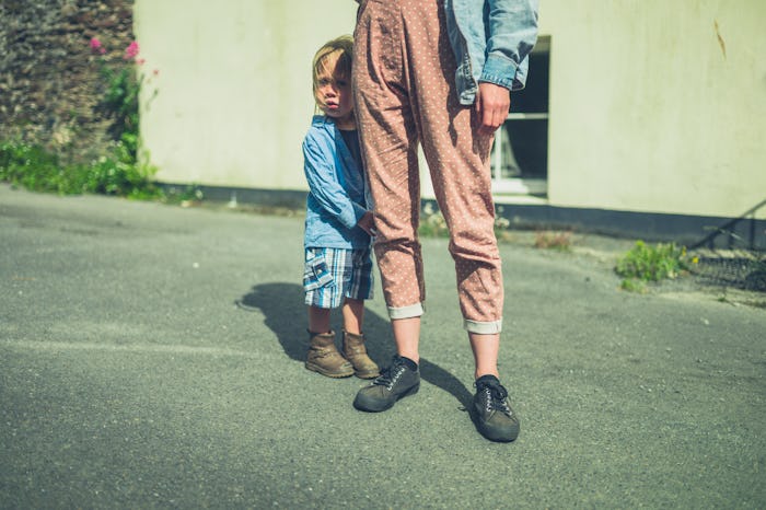 A little toddler is hiding behind his mother in the street