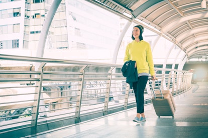 Young female traveler with luggage walking on sky bridge in city, summer vacation and ...