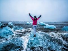 Young woman traveler travel to Diamond Beach in Iceland. Frozen ice on black sand beach known flows ...