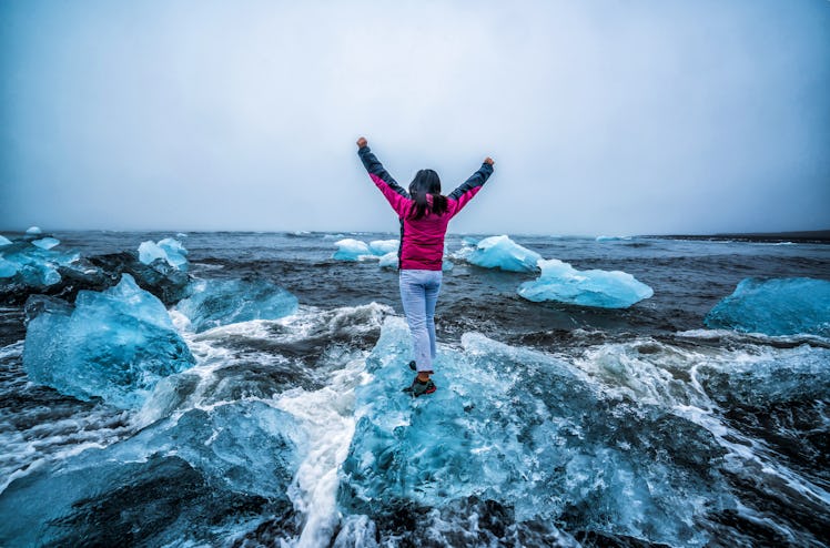 Young woman traveler travel to Diamond Beach in Iceland. Frozen ice on black sand beach known flows ...