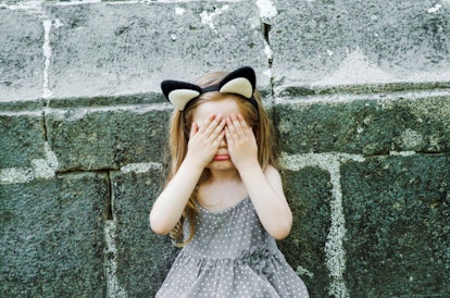 sad toddler girl with hands on face crying,unhappy leaning on stone wall.Anxious lonely disstres chi...
