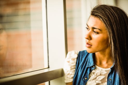 Pretty brunette sitting alone unsmiling against a window